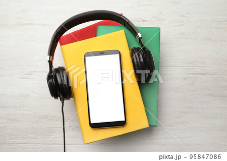 Books with modern headphones and smartphone on white wooden background, top view. Space for design 95847086
