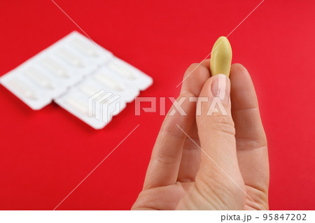 Woman holding suppository on red background, closeup. Hemorrhoid treatment Woman holding suppository on red background, closeup. Hemorrhoid treatment 95847202
