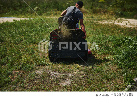 View from the back of an unrecognizable male gardener riding a lawn mower, mowing the green grass in public city park View from the back of an unrecognizable male gardener riding a lawn mower, mowing the green grass in public city park 95847589