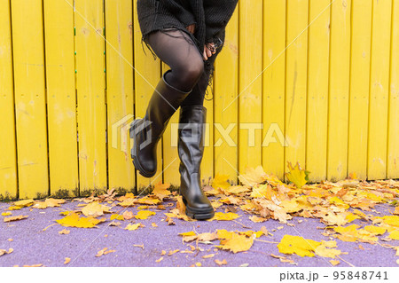 A girl in warm boots poses against a background of fallen foliage 95848741