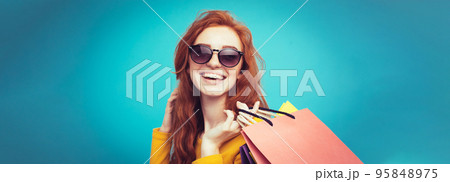 Shopping Concept - Close up Portrait young beautiful attractive redhair girl smiling looking at camera with shopping bag. Blue Pastel Background. Copy space Shopping Concept - Close up Portrait young beautiful attractive redhair girl smiling looking at camera with shopping bag. Blue Pastel Background. Copy space 95848975