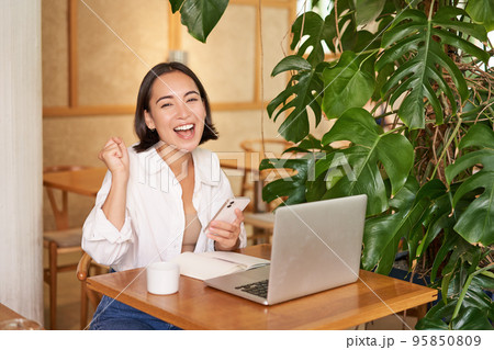 Happy young asian woman feel success, winning and celebrating, sitting with laptop and smartphone in cafe and triumphing, shouting yes Happy young asian woman feel success, winning and celebrating, sitting with laptop and smartphone in cafe and triumphing, shouting yes 95850809