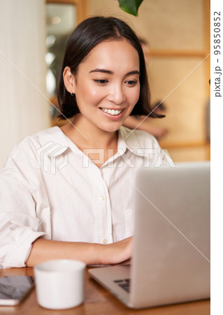 Stylish brunette woman with laptop, sitting in cafe and drinking coffee, smiling happily 95850852