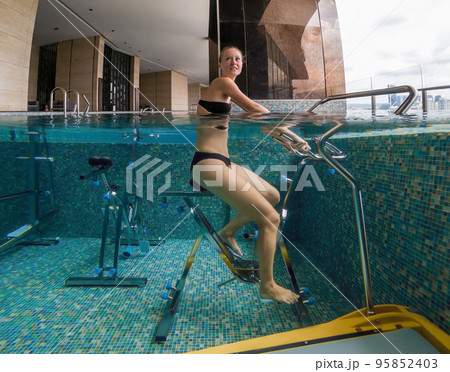 Young woman on bicycle simulator underwater in the pool 95852403