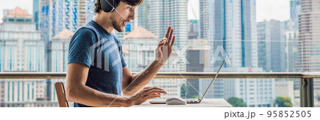 Young man teaches a foreign language or learns a foreign language on the Internet on her balcony against the backdrop of a big city. Online language school lifestyle BANNER, long format Young man teaches a foreign language or learns a foreign language on the Internet on her balcony against the backdrop of a big city. Online language school lifestyle BANNER, long format 95852505