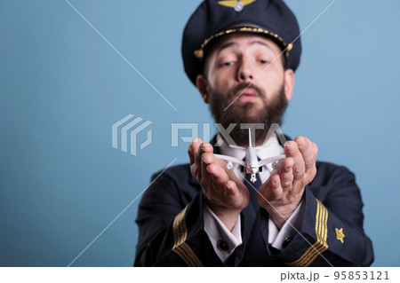 Airplane captain in uniform holding plane model in palms front view, pilot playing with commercial passenger jet toy. Professional aviation academy aviator on blue background 95853121