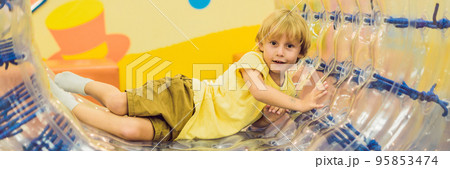 Cute little boy, playing in Zorb a rolling plastic cylinder ring with a hole in the middle, intdoor BANNER, long format 95853474