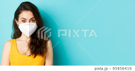 Covid-19, coronavirus and social distancing. Attractive young woman wearing respirator from coronavirus, looking at camera, blue background 95856419