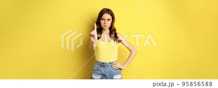 Serious stylish woman showing stop, rejection, prohibition gesture, decline something, disapprove, standing over yellow background Serious stylish woman showing stop, rejection, prohibition gesture, decline something, disapprove, standing over yellow background 95856588
