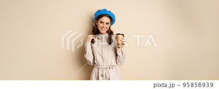 Beautiful modern girl posing with takeout cup of coffee, drinking from reusable cup from cafe and posing happy, beige studio background Beautiful modern girl posing with takeout cup of coffee, drinking from reusable cup from cafe and posing happy, beige studio background 95856939