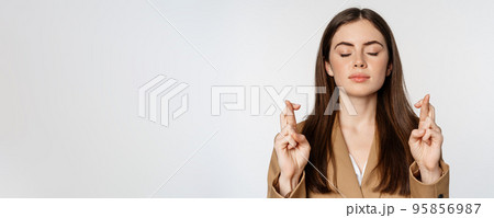 Hopeful saleswoman, corporate woman cross fingers and praying, yearning to achieve smth, standing in suit over white background Hopeful saleswoman, corporate woman cross fingers and praying, yearning to achieve smth, standing in suit over white background 95856987