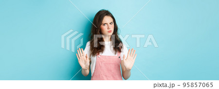 Stop right there. Serious young woman frowning, raising hands and showing block, say no, disapprove bad thing, rejecting you, standing against blue background 95857065