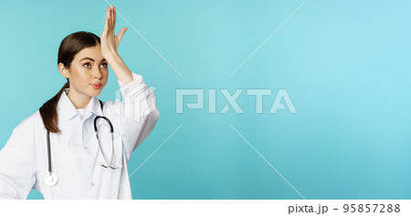 Portrait of annoyed, tired woman doctor, facepalm, roll eyes frustrated, bothered by smth stupid, standing in white coat over torquoise background Portrait of annoyed, tired woman doctor, facepalm, roll eyes frustrated, bothered by smth stupid, standing in white coat over torquoise background 95857288