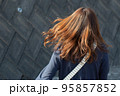 外で髪の毛を揺らしながら歩いている女性の後ろ姿 95857852