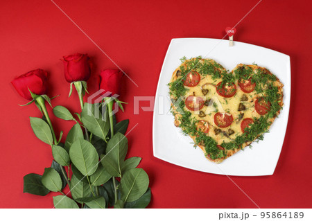 Valentine's day food. Heart shaped pizza next to a red roses, on a red background. Valentine's day concept. Top view. Copy space Valentine's day food. Heart shaped pizza next to a red roses, on a red background. Valentine's day concept. Top view. Copy space 95864189