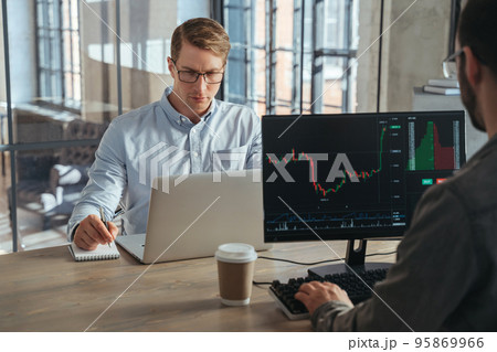 Two stock traders co-working at office sitting at table in front of computers opposite each other Two stock traders co-working at office sitting at table in front of computers opposite each other 95869966