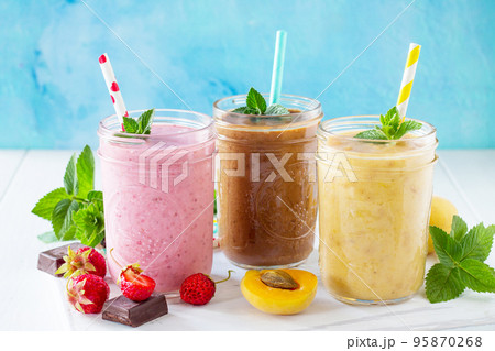 Strawberry, chocolate and apricot smoothie on a white wooden background. Healthy juicy vitamin drink diet or vegan food concept. Strawberry, chocolate and apricot smoothie on a white wooden background. Healthy juicy vitamin drink diet or vegan food concept. 95870268