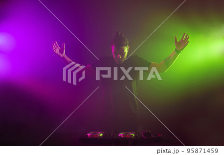 DJ at work mixing sound on her decks at a party or night club with colourful smoke light background DJ at work mixing sound on her decks at a party or night club with colourful smoke light background 95871459