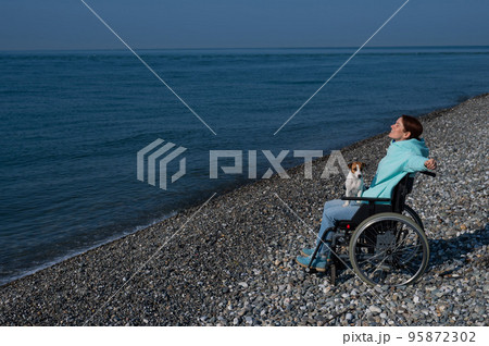 Happy woman in a wheelchair on the seashore raised her hands and imagines that she is flying.  95872302