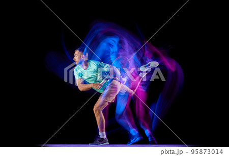 Studio shot of professional tennis player playing tennis isolated over dark background in mixed neon light. Concept of motion, speed, professional sport. 95873014