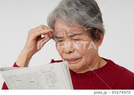 老眼で新聞が読みづらそうなシニア女性 95874970