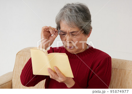 老眼で本が読みづらそうなシニア女性 95874977