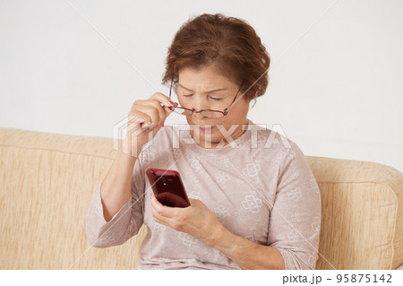 老眼でスマホが見づらそうなシニア女性 95875142