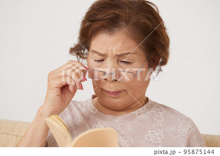 老眼で本が読みづらそうなシニア女性 95875144