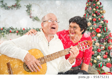 Father playing guitar during christmas. Happy man 60s playing guitar christmas songs. Father playing guitar during christmas. Happy man 60s playing guitar christmas songs. 95875231