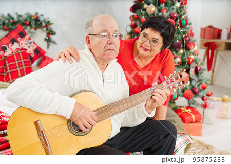 Father playing guitar during christmas. Happy man 60s playing guitar christmas songs. Father playing guitar during christmas. Happy man 60s playing guitar christmas songs. 95875233
