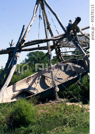 A boat on land is suspended from tree trunks. Vertical photo. A boat on land is suspended from tree trunks. Vertical photo. 95876113