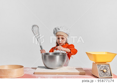 Cute little child, girl in image of chef cooking over grey background. Making dough 95877174