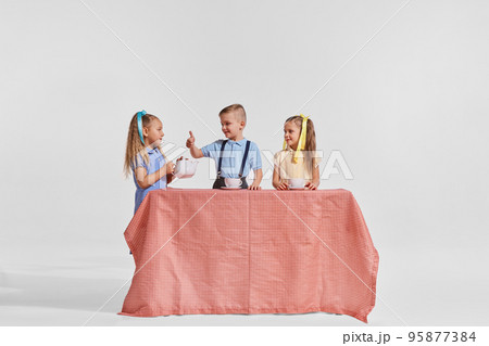 Portrait of three children, boy and girls sitting at the table and drinking tea over grey background. Breakfast time 95877384