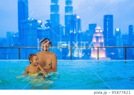 Father and son in outdoor swimming pool with city view in blue sky 95877621
