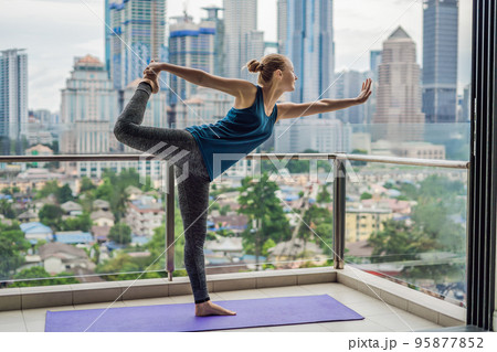 Young woman is practicing yoga in the morning on her balcony with a panoramic view of the city and skyscrapers 95877852