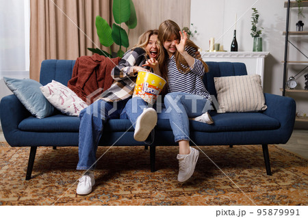 Frightened women watching horror movie and eating popcorn at home 95879991
