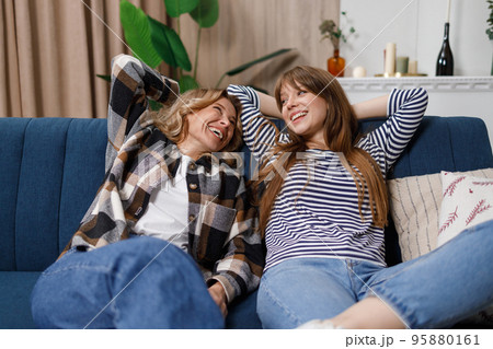 Lazy mother and daughter are lying on the sofa with their hands above their heads. Two women of different ages laughing are relaxing on the couch Lazy mother and daughter are lying on the sofa with their hands above their heads. Two women of different ages laughing are relaxing on the couch 95880161