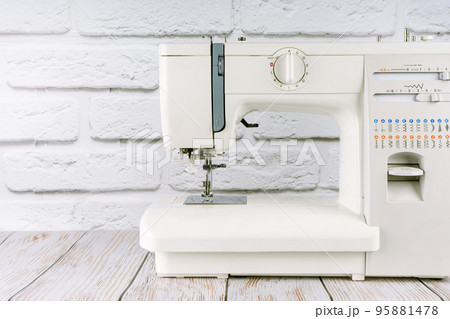 Modern sewing machine on white brick background Modern sewing machine on white brick background 95881478
