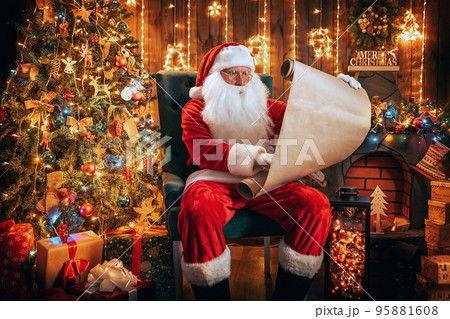 Santa Claus sitting in room decorated for Christmas while reading the wish list of good children  95881608