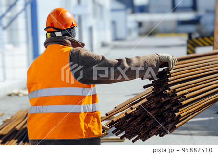 Slinger in construction helmet and orange vest unloads cargo on construction site. View from back 95882510