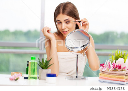 Woman doing morning makeup routine putting mascara in bathroom mirror at home 95884328