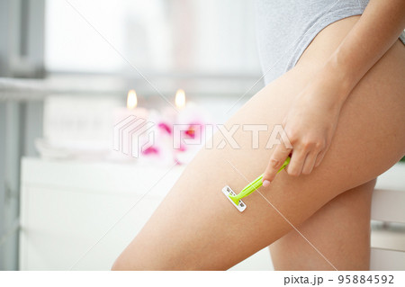 Young woman removing hair on legs with razor at bathroom Young woman removing hair on legs with razor at bathroom 95884592