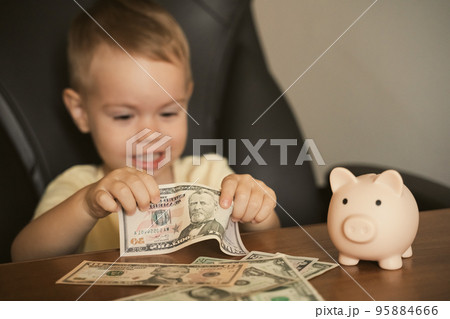 Smart happy child boy holding dollar banknote saving in piggy bank. Saving money in a piggy bank Smart happy child boy holding dollar banknote saving in piggy bank. Saving money in a piggy bank 95884666