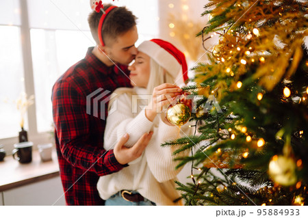 Happy couple decorating christmas tree at home. Smiling Man and Woman together Celebrating Christmas Happy couple decorating christmas tree at home. Smiling Man and Woman together Celebrating Christmas 95884933