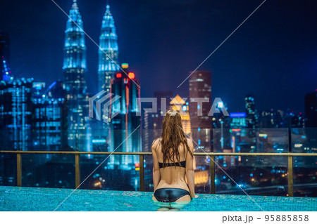 Young woman in outdoor swimming pool with city view at night 95885858