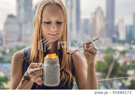 Young woman with mehendi from henna on hand eating chia pudding on her balcony overlooking the big city Young woman with mehendi from henna on hand eating chia pudding on her balcony overlooking the big city 95886273