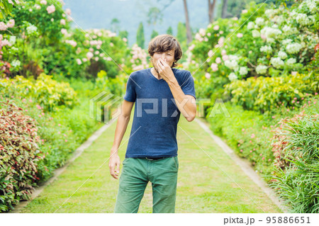 Young man sneeze in the park against the background of a flowering tree. Allergy to pollen concept Young man sneeze in the park against the background of a flowering tree. Allergy to pollen concept 95886651