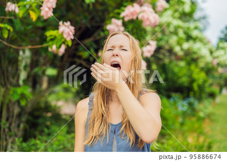 Young woman sneezes in the park against the background of a flowering tree. Allergy to pollen concept 95886674