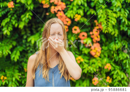 Young woman sneezes in the park against the background of a flowering tree. Allergy to pollen concept Young woman sneezes in the park against the background of a flowering tree. Allergy to pollen concept 95886681
