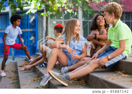 Group of boys and girls sitting on stairs outdoors and chatting 95887142